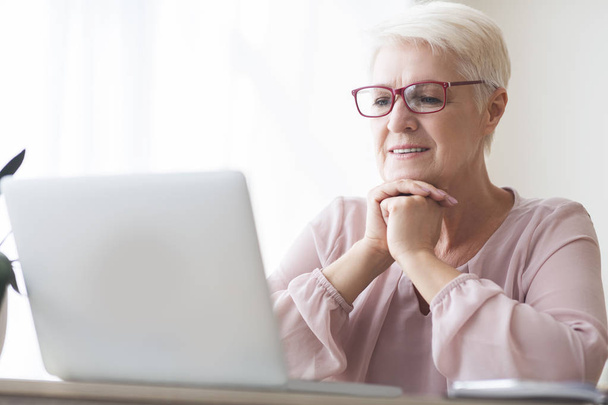 Mujer mayor leyendo artículo en línea, utilizando el ordenador portátil
 - Foto, Imagen