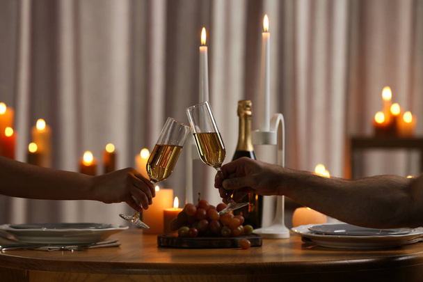 Couple clinking glasses of champagne at table with burning candles, closeup - Foto, imagen