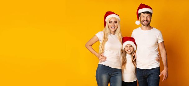 Родители и дочь в шляпах Санта-Клауса, обнимающиеся в студии, Панорама
 - Фото, изображение