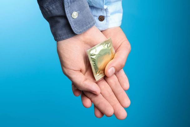 Gay couple with condom on light blue background, closeup - 写真・画像
