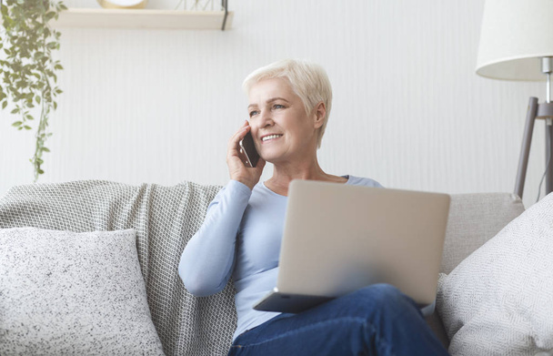 Modern senior woman holding laptop and talking by phone - Foto, Bild