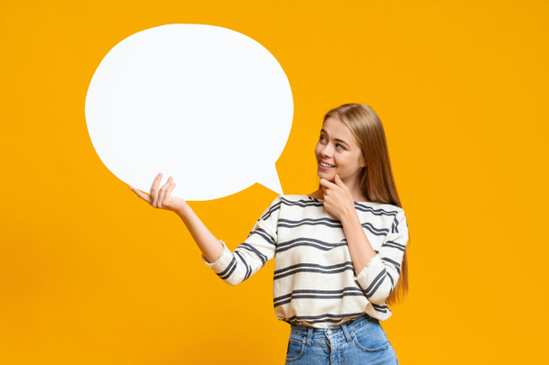 Pensive young girl holding blank speech bubble over yellow background - Photo, Image