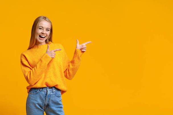 Cheerful teenage girl pointing at copy space on orange background - Photo, image