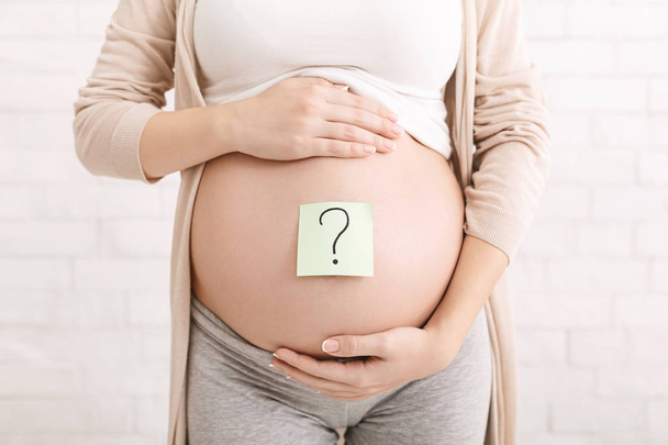 Έγκυος κοιλιά γυναίκα με ερωτηματικό σε αυτοκόλλητα χαρτί - Φωτογραφία, εικόνα