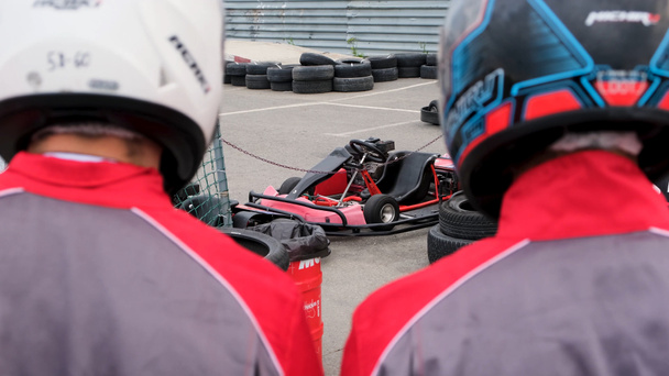 Close up of racer backs wearing special uniforms and helmets going to the kart cars, competition and race concept. Media. Rear view of two men before the karting race. - Photo, Image