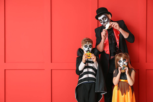 Vader met kinderen in Halloween kostuums eten koekjes op kleur achtergrond - Foto, afbeelding