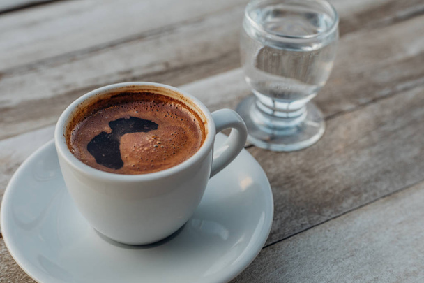 Τούρκος ή ελληνικός ζεστός καφές στο λευκό ρουστίκ ξύλινο τραπέζι με χυμένους κόκκους καφέ. Πρόκειται για παραδοσιακό γευστικό αναψυκτικό ελληνικό ή τούρκικο καφέ από την ελληνική ή τουρκική κουζίνα - Φωτογραφία, εικόνα