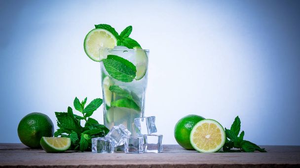 Mojito cocktail tuoretta kalkkia, mintunlehtiä ja jääkuutioita läpinäkyvässä lasissa puupohjalla. Virkistävä alkoholijuoma
. - Valokuva, kuva