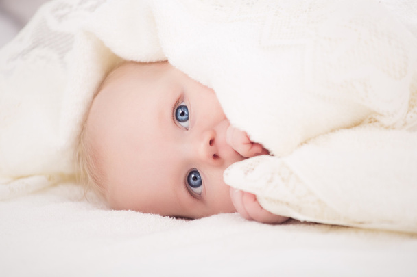 Baby blickt unter einer weißen Decke in die Kamera - Foto, Bild