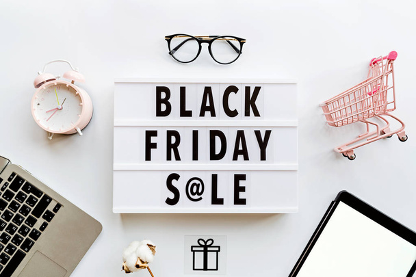 Creative promotion composition Black friday sale text on lightbox on white background, next grocery trolley, credit card, cash money, mobile phone, shopping bag. Flat lay, top view, overhead, mockup - Photo, Image