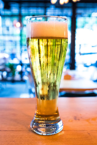 カフェ、レストランやバーで古い木製のテーブルの上にビールのガラス。ナイトライフのコンセプトイメージ。レトロなヴィンテージバーのインテリアで木製の机の上に冷たいビールグラス。このビールはドラフト&ラガーだ.  - 写真・画像