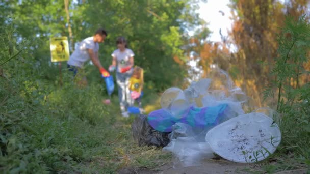 műanyag szennyezés, lány és fiú kisgyermek gyűjti szemetet szemeteszsákba fókuszálatlan, miközben takarítás a szabadban a műanyag és polietilén a zöld fű - Felvétel, videó