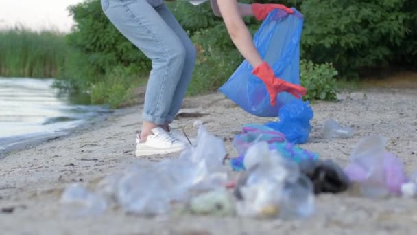Strandreinigung: Aktivistin in Gummihandschuhen sammelt Plastikmüll in Müllsack, während sie Böschung reinigt - Filmmaterial, Video
