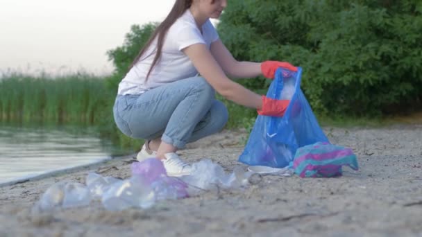 ochrona środowiska, aktywistka w gumowych rękawiczkach zbiera odpady z tworzyw sztucznych i polietylenu do worka na śmieci podczas czyszczenia brzegu - Materiał filmowy, wideo