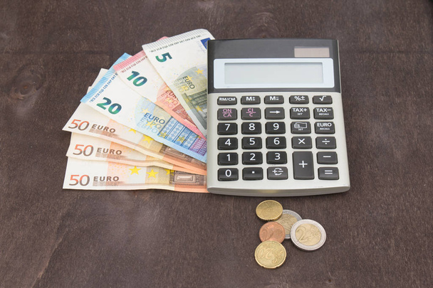 Bankovky a mince s kalkulačkou. Eurobankovky na dřevěném pozadí. Fotografie pro daně, zisk a náklady. 50 euro, 20 euro, 10 euro. Peníze a finance - Fotografie, Obrázek