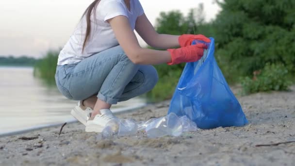 Çöp toplama, lastik eldivenli gönüllü kadın çöp torbasında plastik çöp toplarken sahili temizliyor. - Video, Çekim