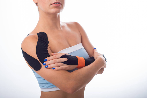 Female shoulder with kineziotape on a white background. Alternative medicine for sports injuries of joints and ligaments. Young sportswoman with medical record on a sore shoulder and wrist. - Foto, Imagem