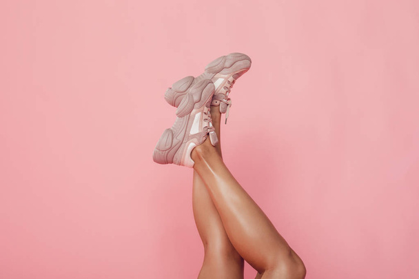 Female legs in sneakers on a pink background. - Zdjęcie, obraz