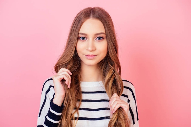 portrait of a young and attractive teenager long-haired woman stylish model in a striped sweater in studio on a pink background . concept of healthy, strong and thick hair - Foto, afbeelding