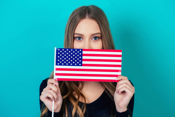 スタジオの青い背景にアメリカ国旗を手にした魅力的な少女の肖像画。アメリカ独立記念日の概念7月4日 - 写真・画像