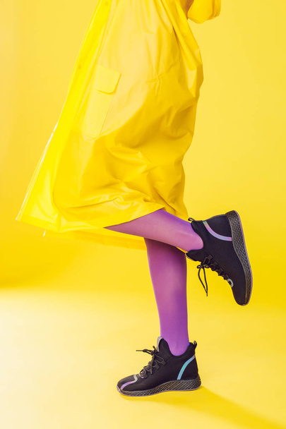 Frauenbeine in lila Strumpfhosen und Turnschuhen auf gelbem Hintergrund. - Foto, Bild