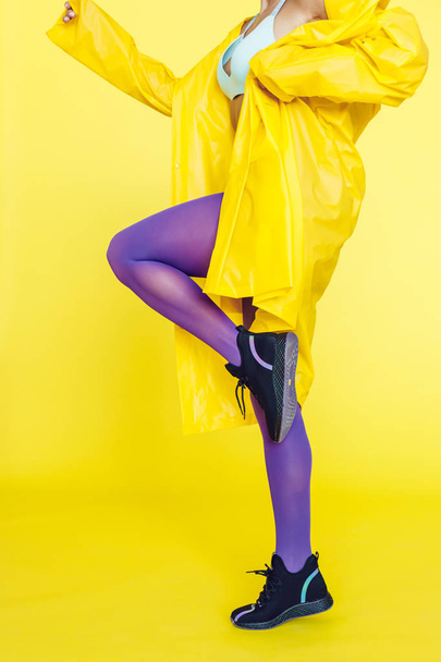 Female legs in purple tights and sneakers on a yellow background. - Fotoğraf, Görsel