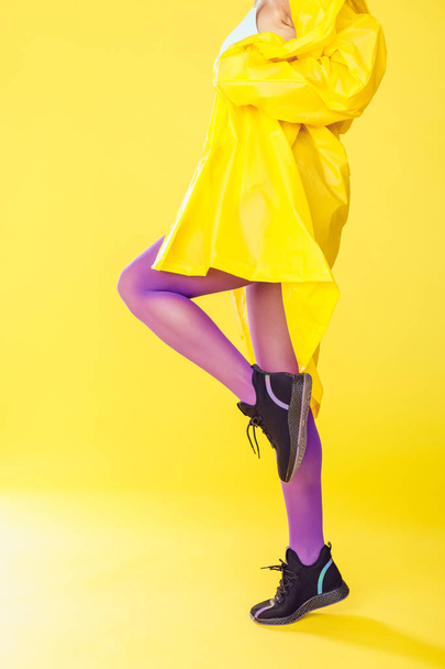 Female legs in purple tights and sneakers on a yellow background. - Photo, image
