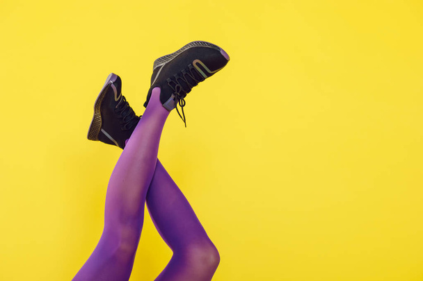 Female legs in purple tights and sneakers on a yellow background. - Fotó, kép