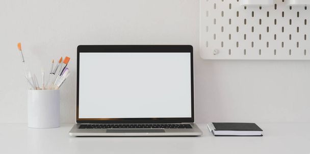 minimaler Künstler-Arbeitsplatz mit leerem Bildschirm-Laptop und Dekorationen auf weißem Tisch  - Foto, Bild