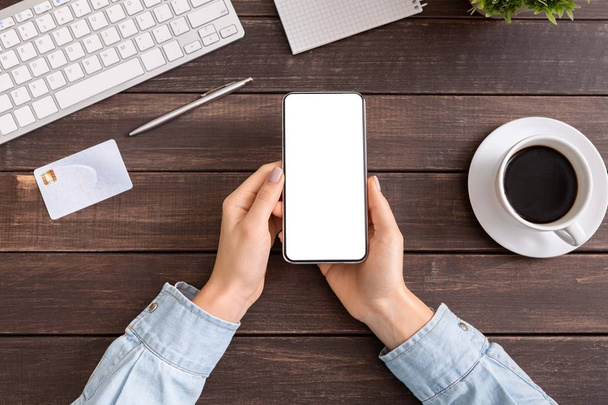 Manos de mujer sosteniendo teléfono inteligente con pantalla blanca en blanco en la oficina
 - Foto, imagen
