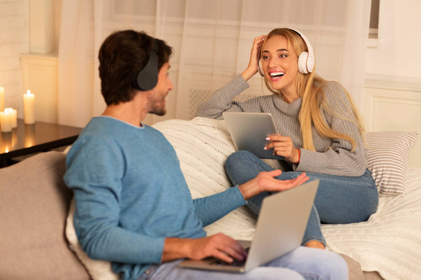 Spouses Using Laptop And Tablet Wearing Headphones Relaxing At Home - Photo, Image