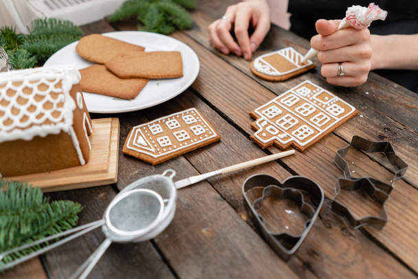 Πολλά μπισκότα τζίντζερ υπό μορφήν ευρωπαϊκούς οίκους στο καφετί ξύλινο τραπέζι. Διακόσμηση με το λευκό γλυκό λούστρο. Χριστουγεννιάτικη διάθεση, χειμωνιάτικο πρωινό. - Φωτογραφία, εικόνα