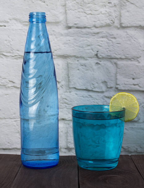 Un bicchiere blu e una bottiglia d'acqua agua pura con un cerchio di limone Un concetto di acqua pura che porta vita e salute
 - Foto, immagini