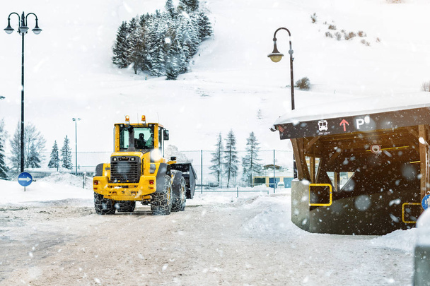 große Lademaschine mit Stahlmetallketten entfernt im Winter große Schneehaufen von der Stadtstraße im alpinen Gebirge. Nachwirkungen starker Schneefälle. Niederschlagsreinigungsanlagen - Foto, Bild