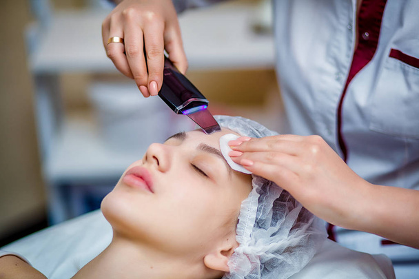 Žena přijímá ultrazvukové obličeje odlupování na kosmetologie salon. Postup čištění ucpané póry, ultrazvukové ošetření pro omlazení pleti, kosmetička používá moderní přístroje pro aktualizaci - Fotografie, Obrázek