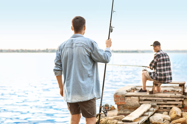 Genç adam ve babası nehirde balık tutuyor. - Fotoğraf, Görsel