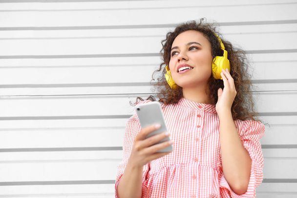 Прекрасна афро-американська жінка з мобільним телефоном слухає музику на відкритому повітрі. - Фото, зображення