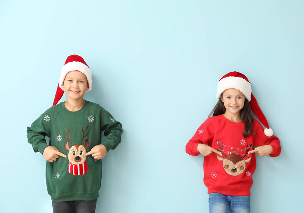 Bambini piccoli in maglioni di Natale e cappelli di Babbo Natale su sfondo di colore
 - Foto, immagini
