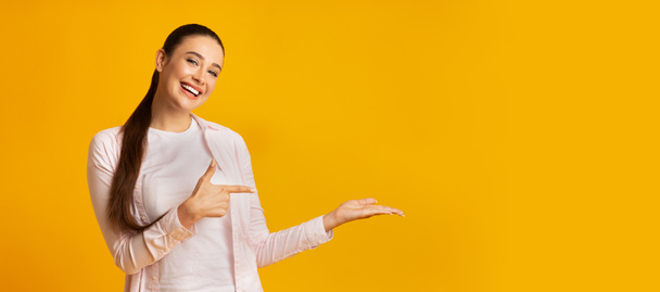 Vrolijk meisje wijzend vinger houden iets op gele achtergrond - Foto, afbeelding