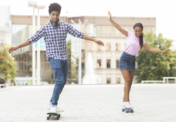Cheerful teenagers racing on skateboards against cityscape - Foto, Bild