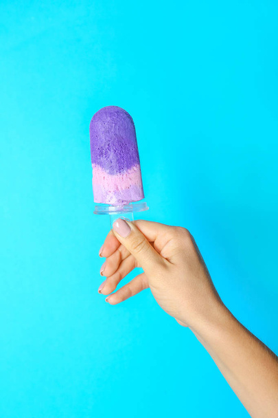 Female hand with tasty blueberry ice cream on color background - Valokuva, kuva