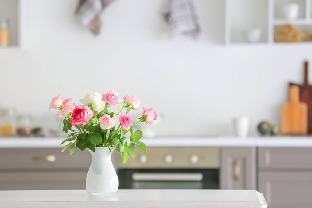 Beautiful rose flowers in vase on table in kitchen - Fotoğraf, Görsel
