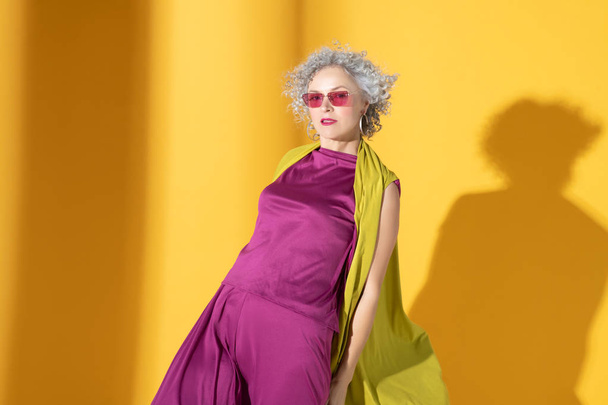 Curly grey-haired woman wearing pink suit and glasses - Фото, изображение