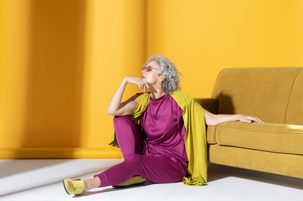 Curly woman in pink suit sitting on the floor near sofa - Фото, зображення