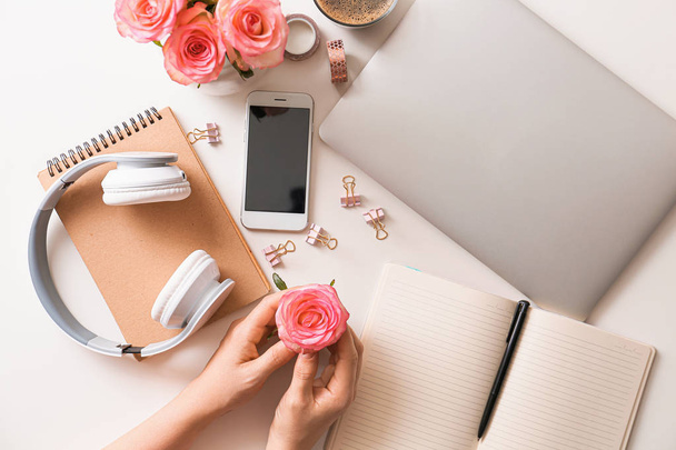 Kobiece ręce z pięknymi kwiatami róż, laptop, telefon komórkowy i słuchawki na białym tle - Zdjęcie, obraz