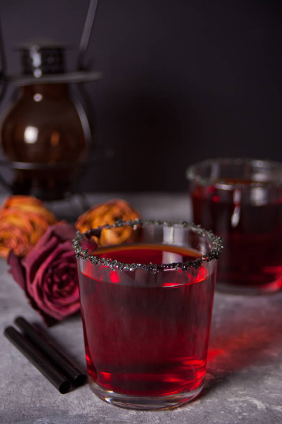 Twee glazen met rode cocktail, gedroogde rozen voor Halloween Party op de donkere achtergrond - Foto, afbeelding