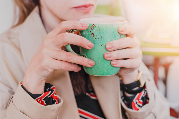 Duży mięta zielona herbata filiżanka w rękach kobiet pastelowy manicure siedząc w kawiarni. - Zdjęcie, obraz