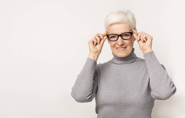 Bella donna anziana cercando nuovi occhiali e cercando di fotocamera
 - Foto, immagini