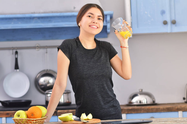 A sports asian woman in a black t-shirt prepares Breakfast and drinks fresh orange juice. - Photo, Image