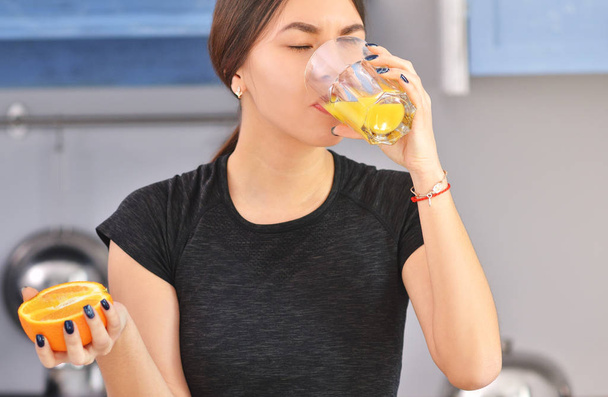 Sport Asian woman in a black t-shirt makes and drinks orange juice in the kitchen. - Foto, immagini